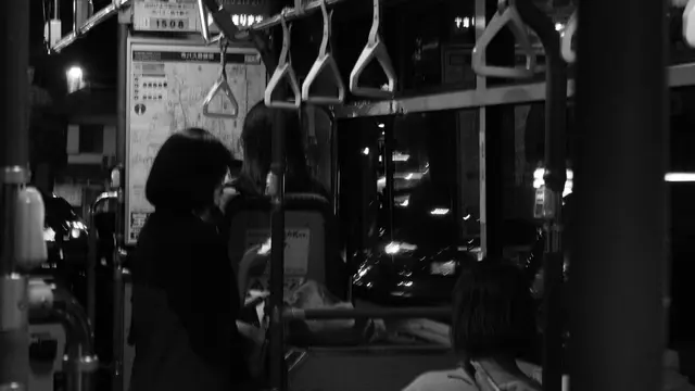 Night bus interior, hand straps and city lights outside
