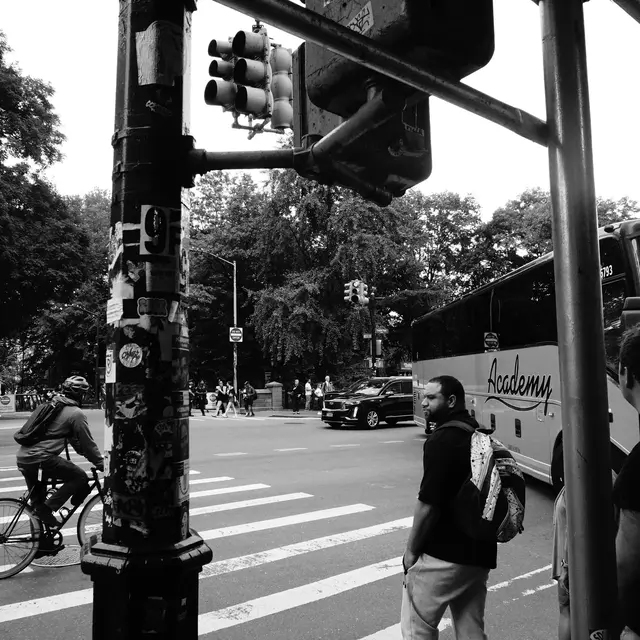 Stickered pole, cyclist and Academy bus at a Central Park crossing