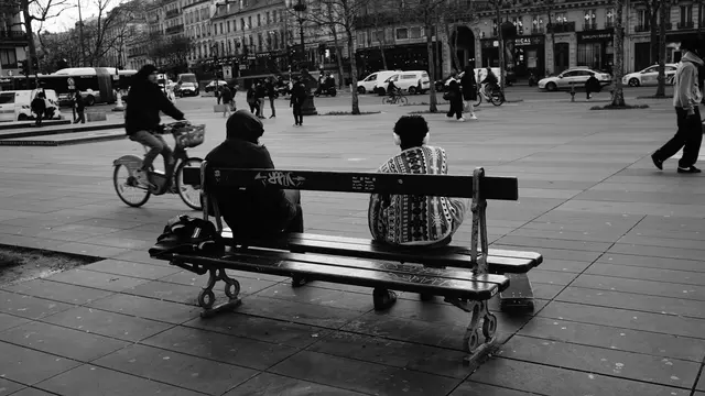 Two friends on a bench, one in headphones, watching the square