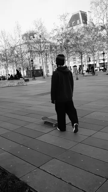 Skater in a beanie rolling away toward the mansard rooftops