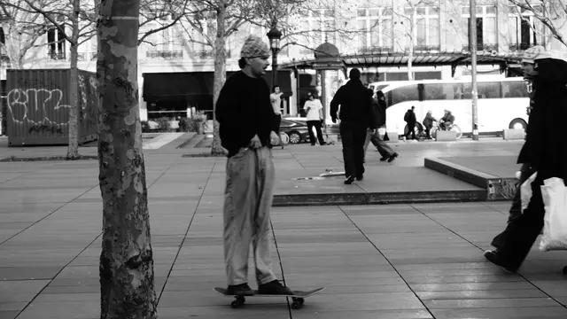 Skater in a bandana behind a plane tree, metro entrance beyond