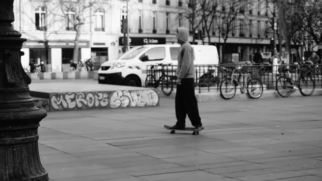 Hooded skater gliding past a graffiti ledge and parked bikes