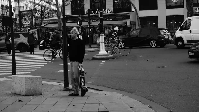Skater waiting at the crossing, board upright, traffic passing