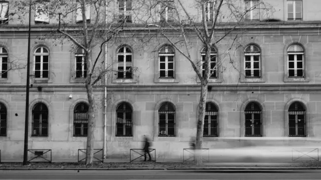 A blurred figure walking past an arched stone façade
