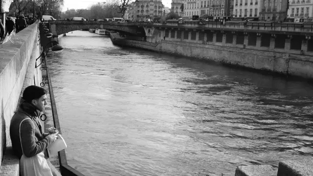A man eating by the Seine, quay and bridge behind