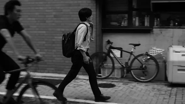 Man walking past a brick wall, cyclist in the foreground