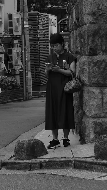 Woman checking her phone by a stone wall, Loewe sign behind