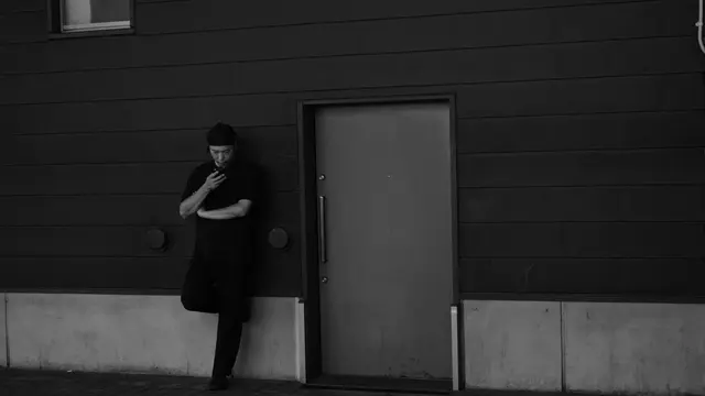 Cook on a break, leaning on the back wall with his phone