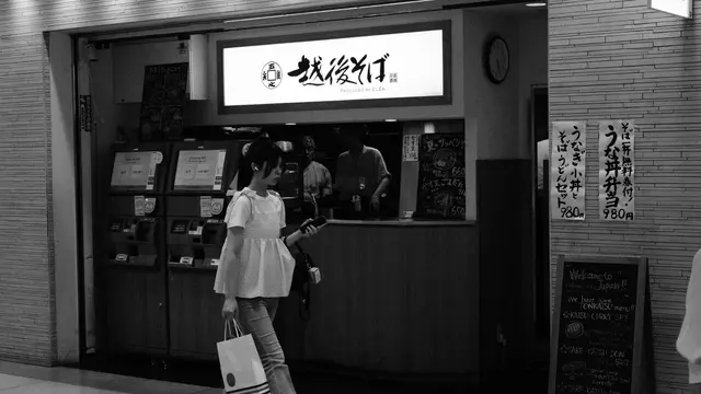 Passerby in front of an Echigo soba stand, ticket machines aglow